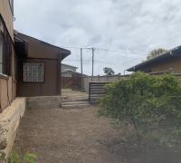  “Vista del patio lateral despejado, donde se observa la primera vivienda de un piso y la segunda vivienda de dos niveles al fondo.