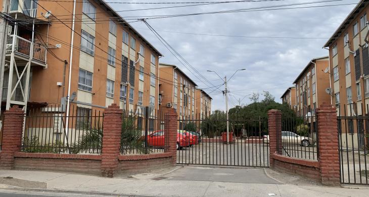  Fotografía del acceso principal del condominio, con entrada vehicular amplia, portón metálico y muros perimetrales de ladrillo que aportan seguridad y privacidad.